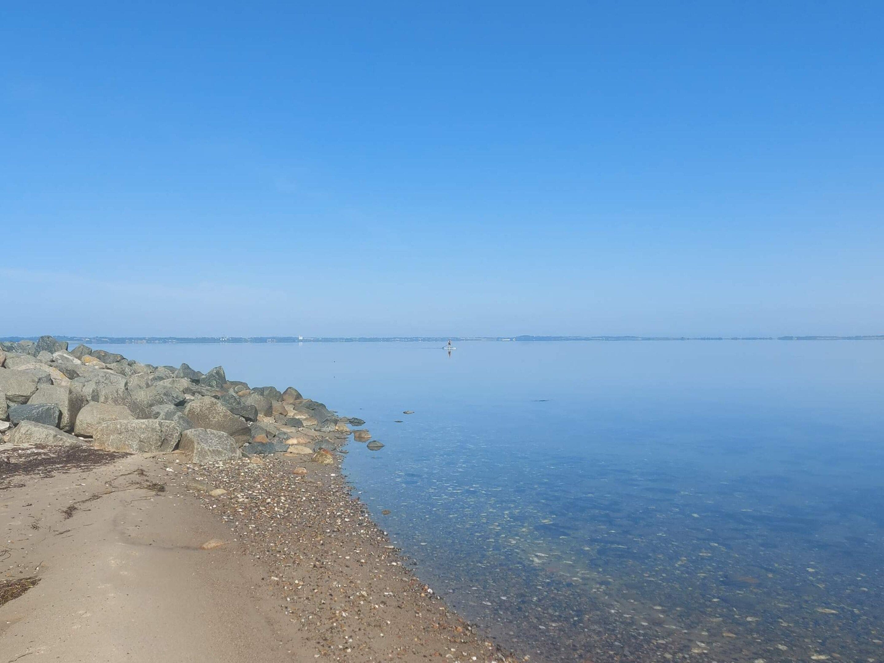 A calm waterfront with a rocky shoreline and a clear sky.