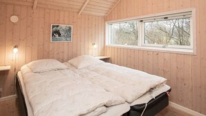 A wooden-paneled bedroom with a bed, bedside lamps, a window, and a framed picture on the wall.