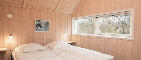 A wooden-paneled bedroom with a bed, bedside lamps, a window, and a framed picture on the wall.