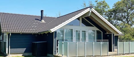 A modern house with a sloped roof, large windows, and a covered patio area.