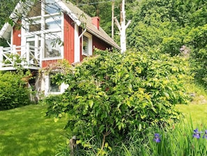 Uma casa vermelha com varanda branca e um jardim verdejante.