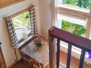 Una mesa de comedor de madera con un florero, una ventana con cortinas y vistas al exterior.