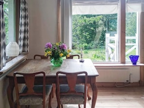 Una mesa de comedor con cuatro sillas, un florero con flores y vistas al verdor exterior.