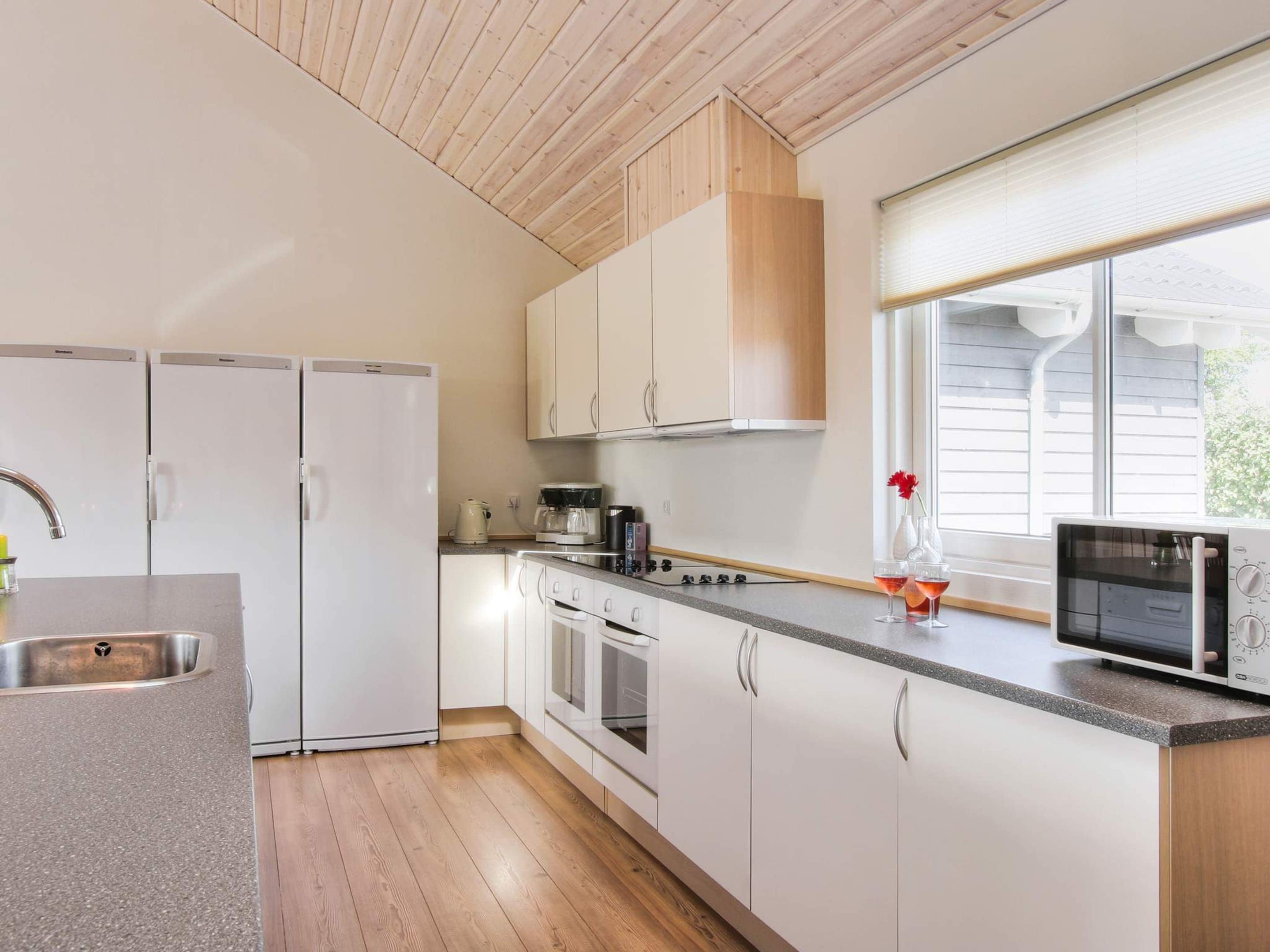 A modern kitchen with white cabinets, a stainless steel sink, a microwave, and a window providing natural light.