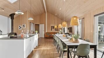 A modern kitchen with a central island, pendant lighting, and a dining area with a long table and chairs.