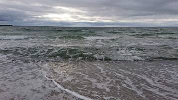 A beach with waves approaching the shore under a cloudy sky.
