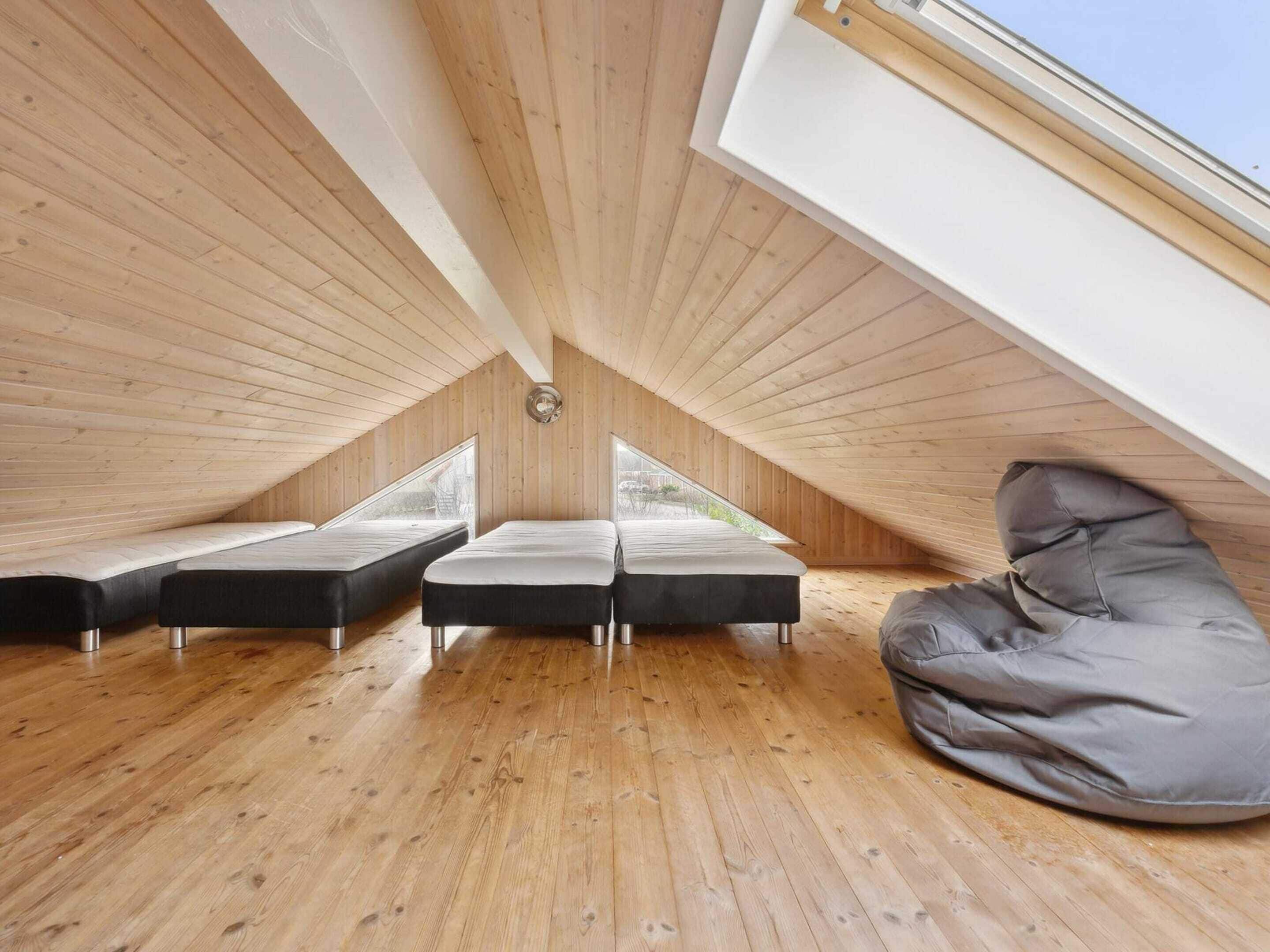 Een zolderkamer met hoge plafonds, houten vloeren, twee bedden, een slaapzak en dakramen.