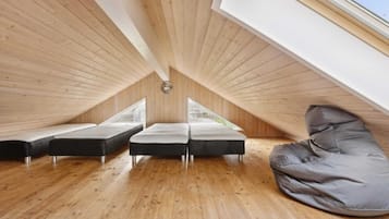 Een zolderkamer met hoge plafonds, houten vloeren, twee bedden, een slaapzak en dakramen.