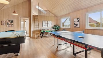 A wooden-paneled room with pool tables, a foosball table, and a ping pong table.