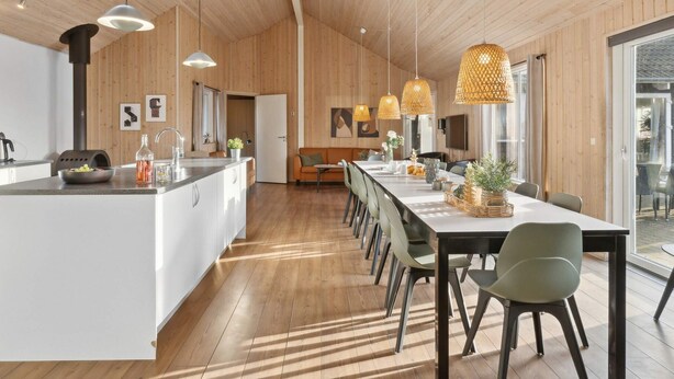 A modern kitchen with a central island, pendant lights, and a dining area with a long table and chairs. - 4 Star Holiday Home in Bagenkop (Sydlangeland)