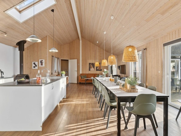 A modern kitchen with a central island, pendant lights, and a dining area with a long table and chairs.