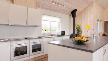 A modern kitchen with white cabinetry, a central island, a built-in oven, and a black stove.