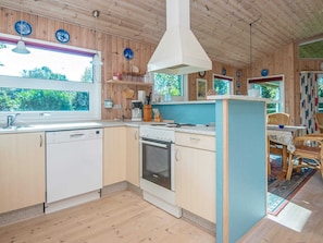 En stuga med träinredning, inklusive ett köksområde med en diskmaskin, spis och diskho från Bosch.