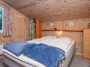 Et rum med træpaneler, seng, sengebord og væglampe.