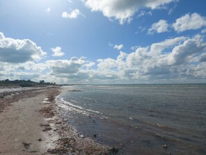 A beach with a wide sandy shore and calm water, under a partly cloudy sky.