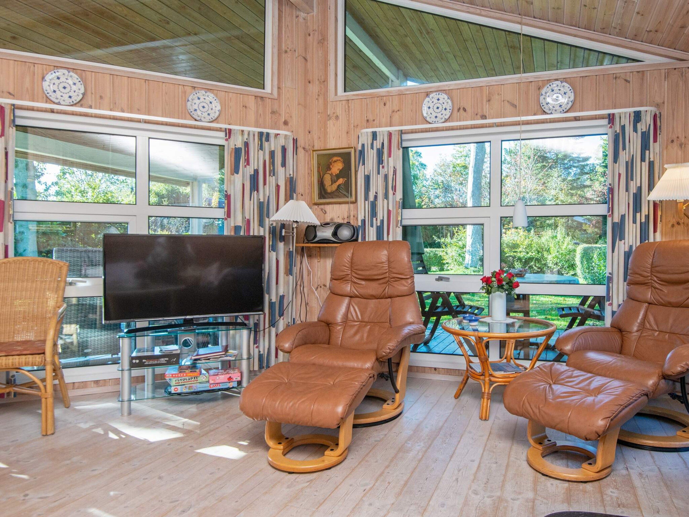 A room with a TV, two leather chairs, a wicker chair, and a table with a vase of flowers.