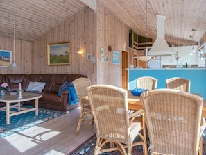 Ein Holzinterieur mit einer Couch, Korbstühlen, einem Esstisch und einer Küchenzeile.
