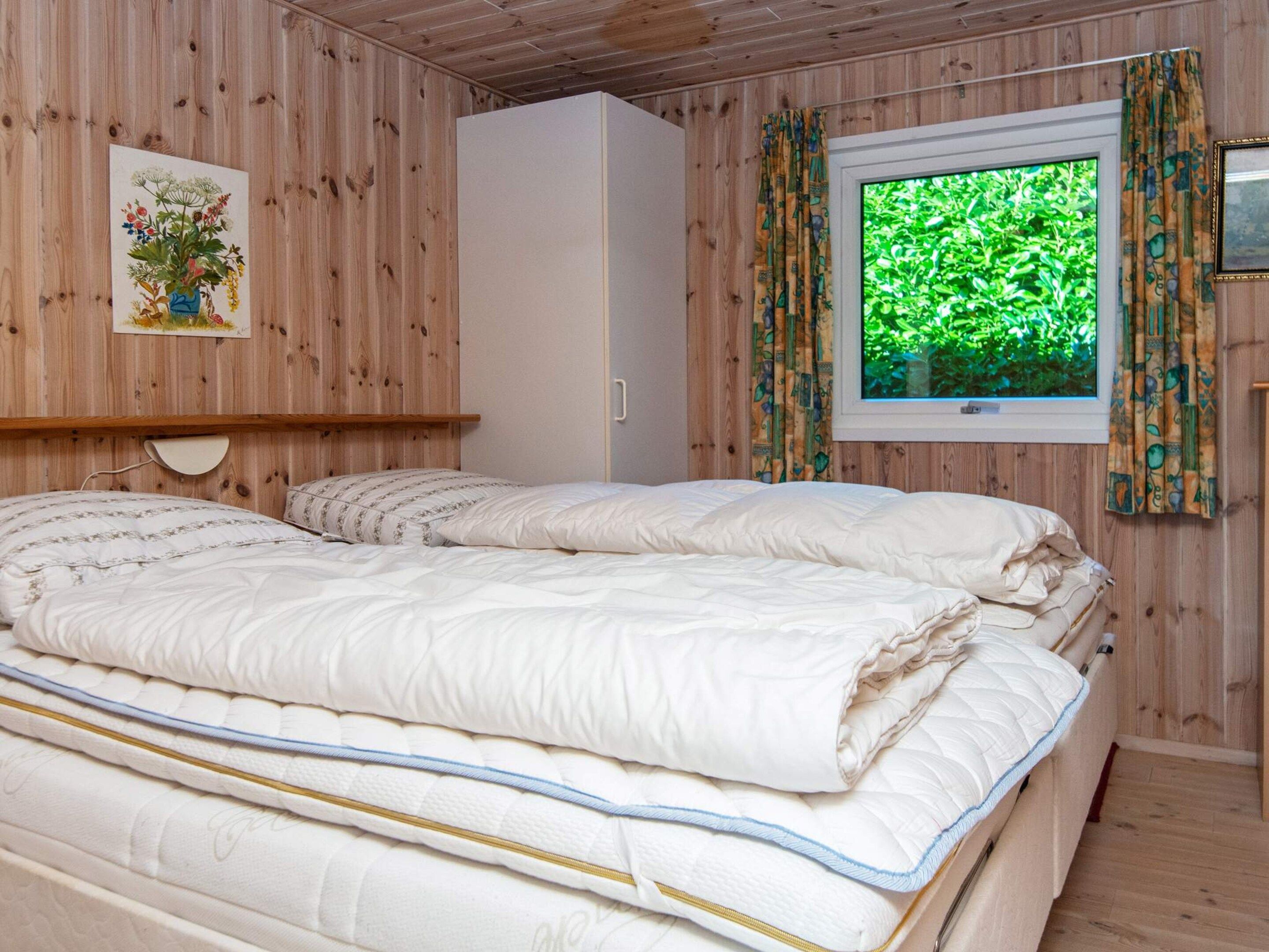 Ein Schlafzimmer mit zwei Betten, einem Kleiderschrank, einem Gemälde und einem Fenster mit Vorhängen.