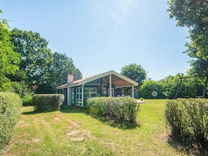A house with a covered porch, surrounded by well-maintained hedges and a grassy yard. - 4 Star Holiday Home in Glesborg (Glesborg)