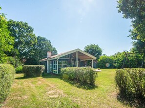 A house with a covered porch, surrounded by well-maintained hedges and a grassy yard. - 4 Star Holiday Home in Glesborg (Glesborg)