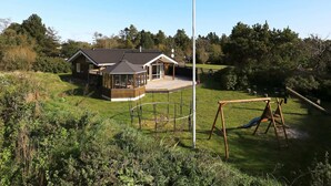 A house with a large deck, a swing set, and a tall flagpole.