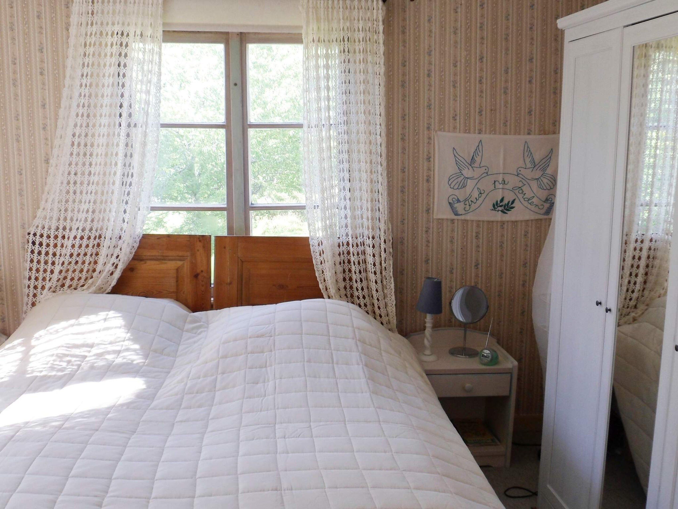 A bedroom with a bed, a nightstand, a lamp, a mirror, and a wardrobe.