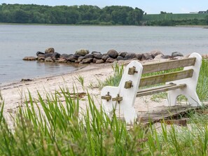 A bench by a lake with a rocky shoreline and greenery in the foreground. - 4 Star Holiday Home in Hejls (Hejls)