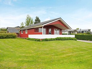 A red single-story house with a white porch, surrounded by a well-maintained lawn and a hedge. - 4 Star Holiday Home in Hejls (Hejls)