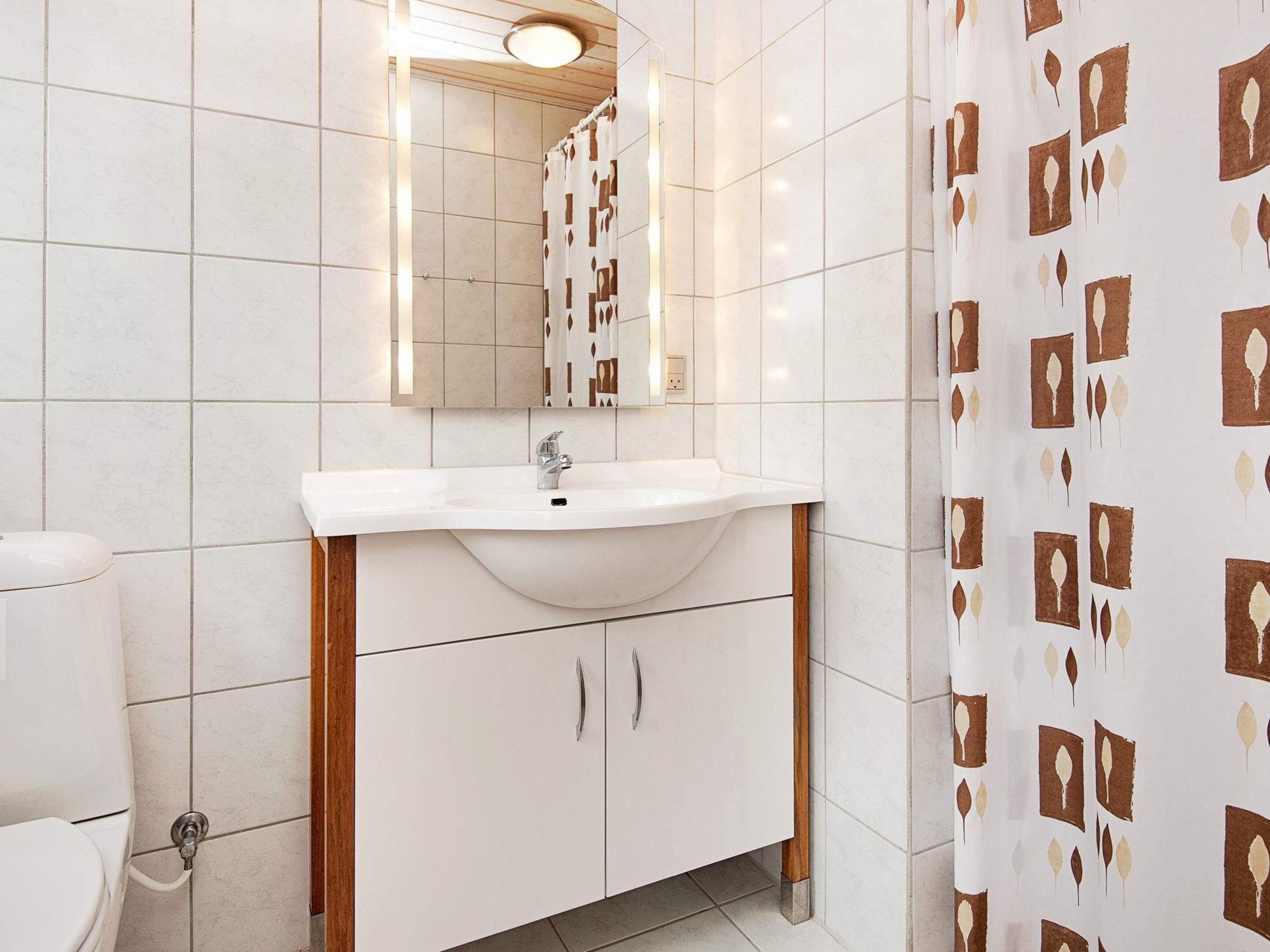 A bathroom with a white sink, mirror, and shower curtain with a leaf pattern.