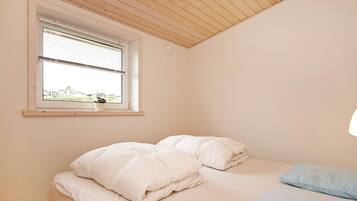 A bedroom with a bed, pillows, a window, and a view of greenery outside.
