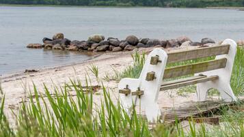 A bench by a lake with a rocky shoreline and greenery in the foreground.
