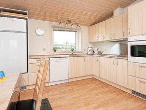 A modern kitchen with wooden cabinets, a dishwasher, a refrigerator, a window with plants, and a sink. - 4 Star Holiday Home in Hejls (Hejls)