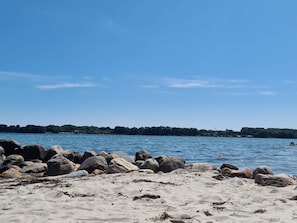 Uma praia com pedras grandes em primeiro plano e um mar calmo.