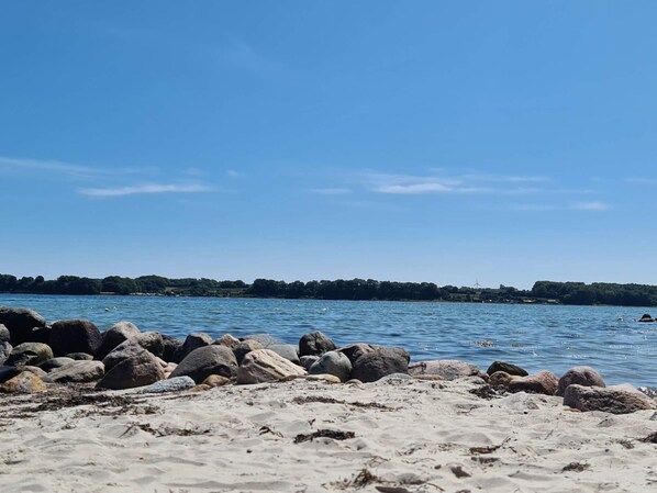 A beach with large rocks in the foreground and a clear blue sky.
