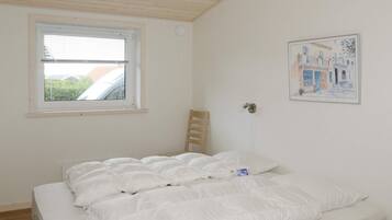 A bedroom with a bed, a window, a chair, and a wall-mounted light fixture.