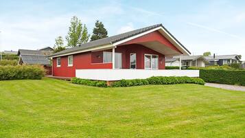 A red single-story house with a white porch, surrounded by a well-maintained lawn and hedges.