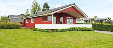 A red single-story house with a white porch, surrounded by a well-maintained lawn and hedges.