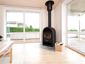 A modern interior with a black wood-burning stove, large windows, and a wooden floor.