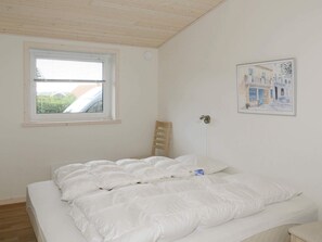 Une chambre à coucher avec un lit, une fenêtre, une chaise et un luminaire fixé au mur.