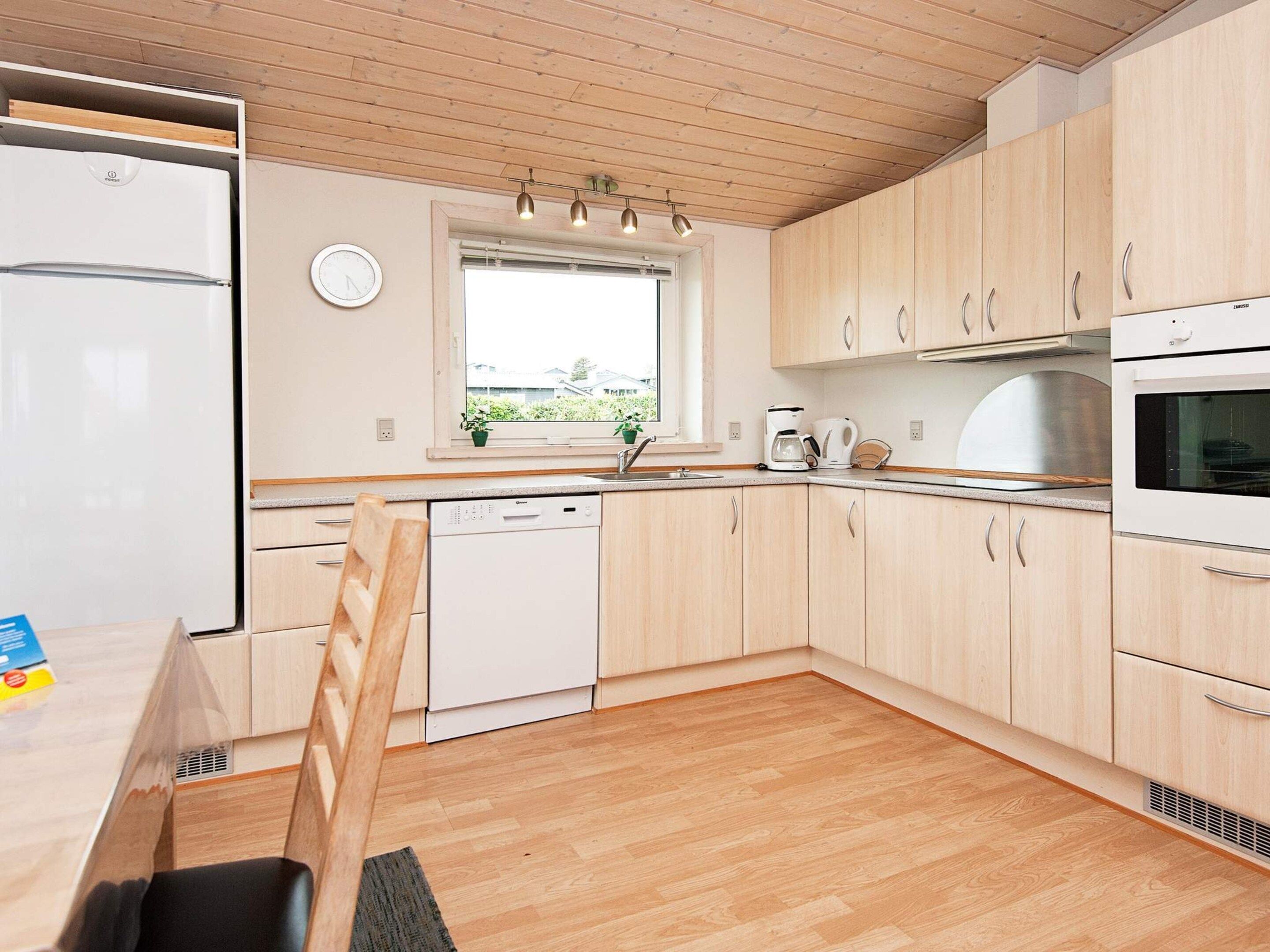 A modern kitchen with wooden cabinets, a built-in dishwasher, a refrigerator, and a window with plants.