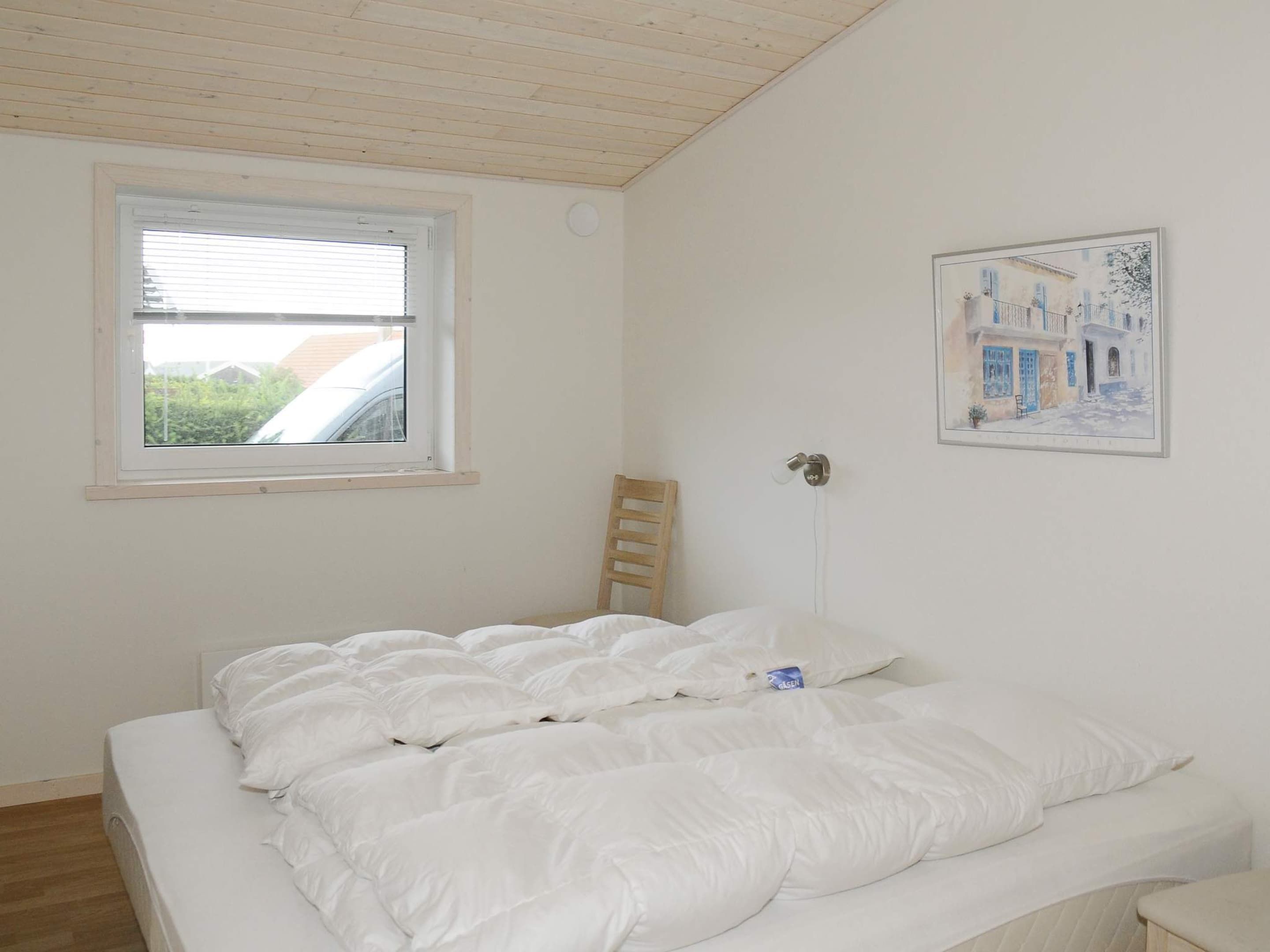 A bedroom with a bed, a window, a chair, and a wall-mounted light fixture.