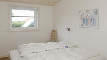 A bedroom with a bed, a window, a chair, and a wall-mounted light fixture.