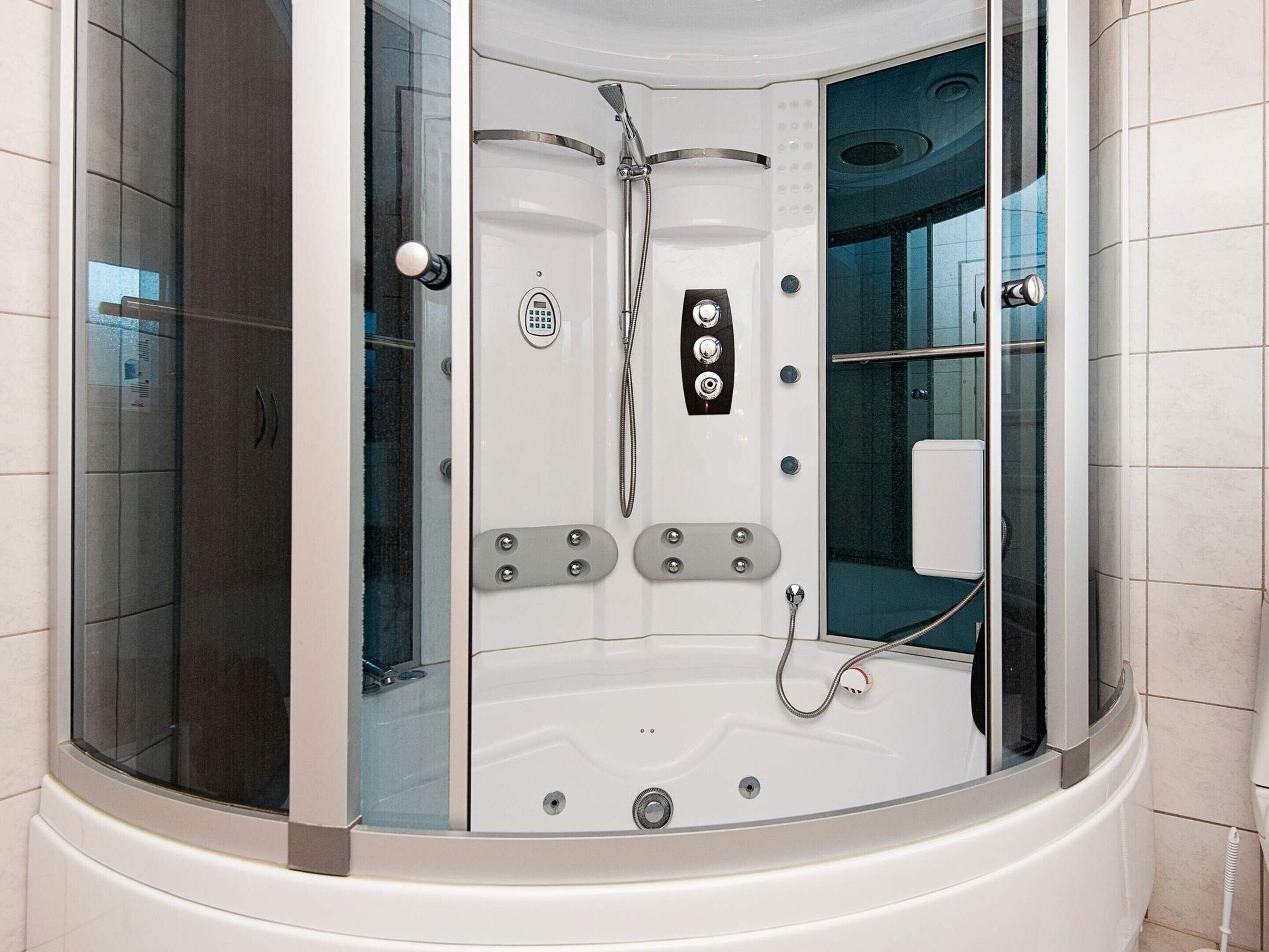 A modern, enclosed shower area with a control panel, a handheld showerhead, and a built-in seat.