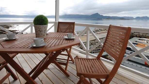 Une terrasse en bois avec une table et des chaises, une plante en pot et une vue sur la mer et les montagnes.