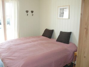 A bedroom with a bed, two pillows, a framed picture on the wall, and a window with curtains. - Holiday Home in Ã…ram (Vanylven)