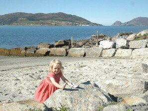 A rocky beach with a child playing, large boulders, and a distant view of hills and water. - Holiday Home in Ã…ram (Vanylven)
