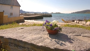 Une vue sur la côte, avec un bâtiment blanc, une jetée en pierre et un pot de fleurs posé sur un rocher.