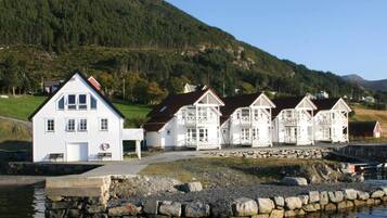A row of white buildings with a stone wall in front, set against a hillside.