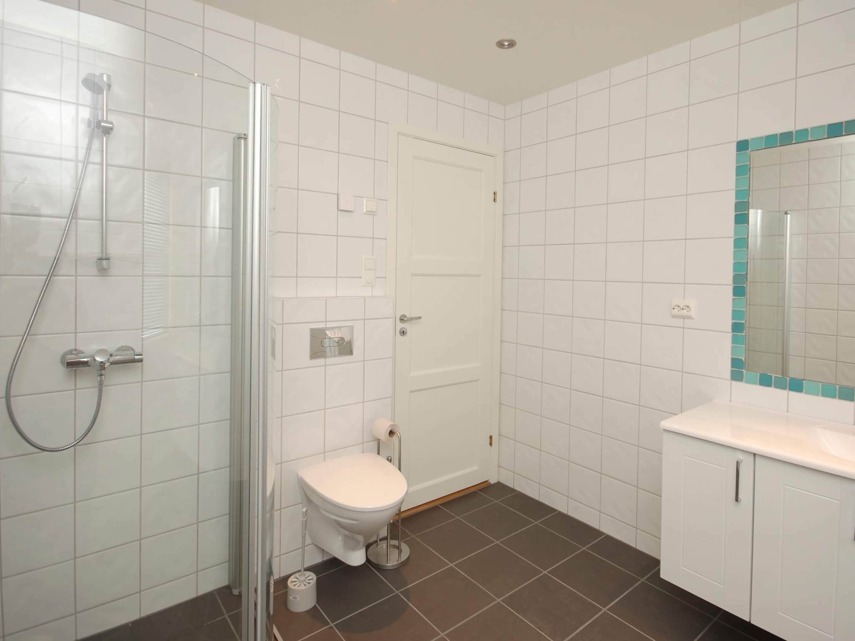 Un bagno con cabina doccia in vetro, un WC bianco, un lavandino con specchio e pavimento piastrellato.