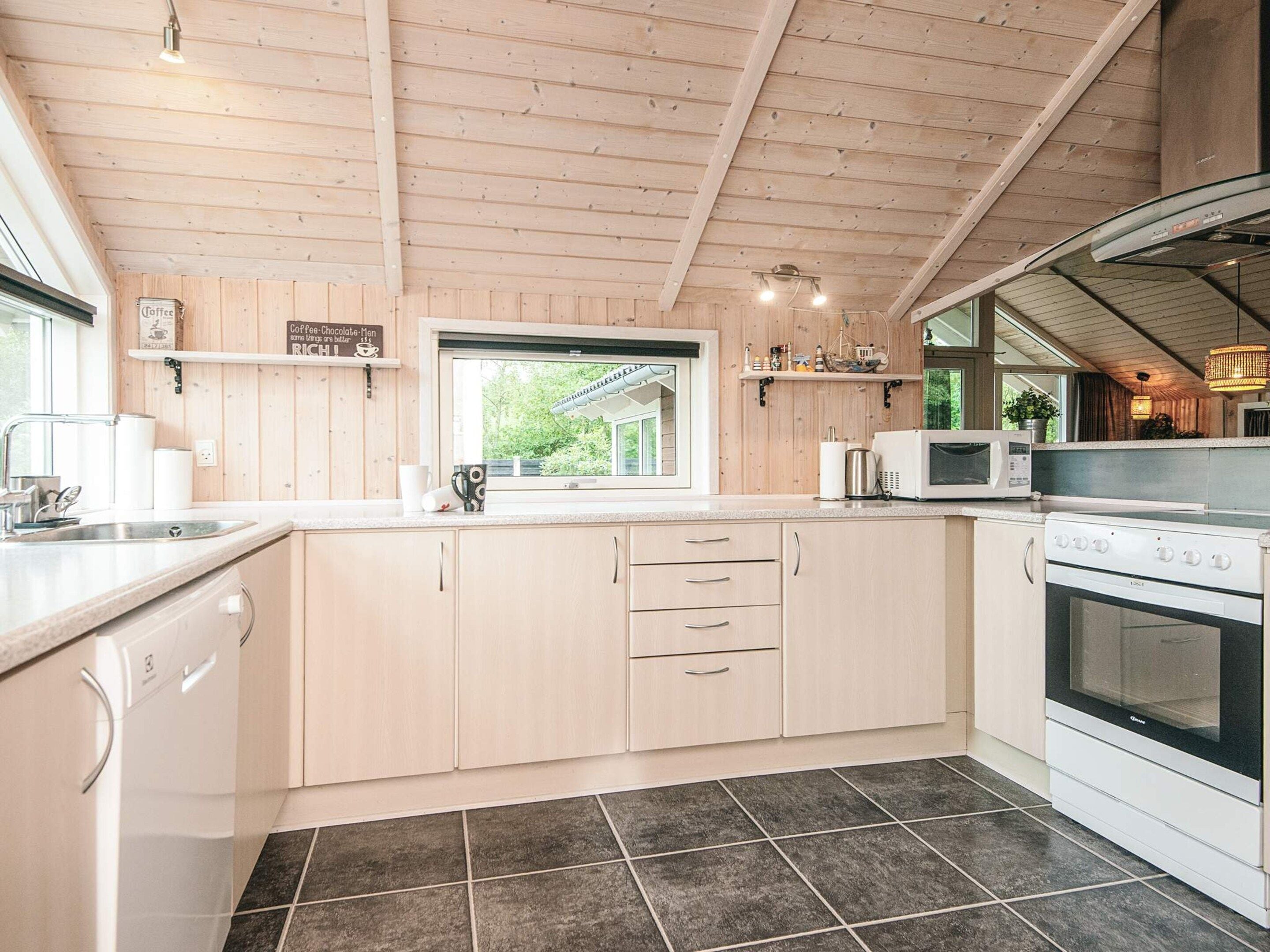 A modern kitchen with wooden cabinets, a built-in oven, a microwave, and a window overlooking greenery.